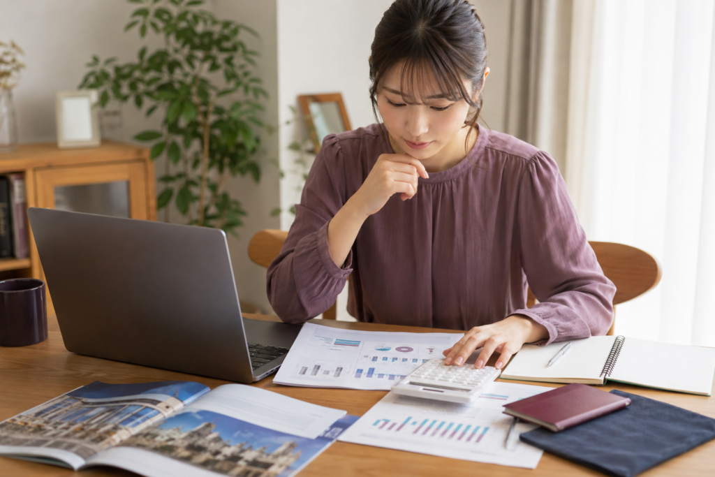 パソコンと電卓を使って海外留学の費用を確認する日本人女性